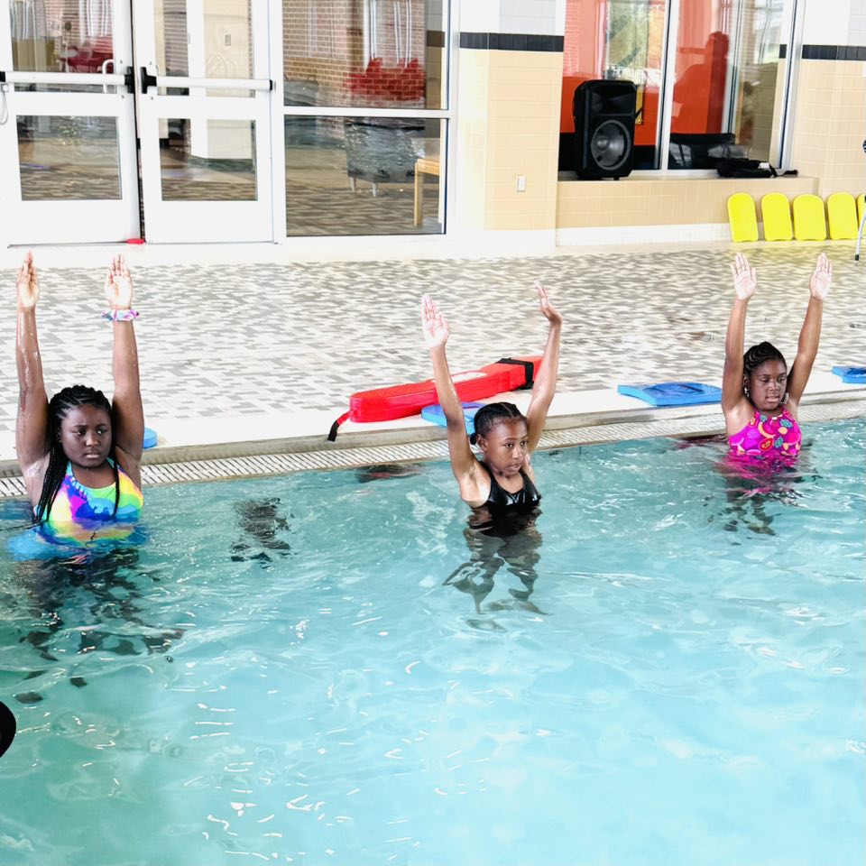 Three girls standing in a pool with their arms up.